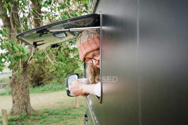 Woman looking out of her camper window smiling enjoying a cup of tea — Stock Photo