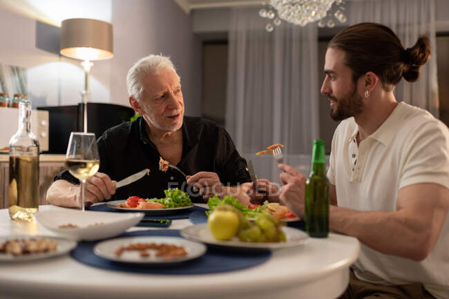 Großvater und Enkel unterhalten sich, während sie zu Hause beim Abendessen frisches Essen genießen — Stockfoto