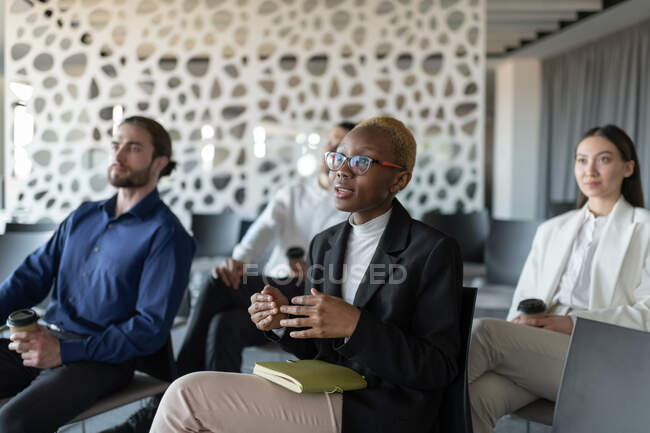 Preto feminino gerente falando enquanto sentado perto colegas durante conferência — Fotografia de Stock