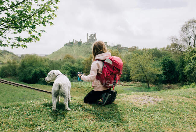 Девушка сидела со своей собакой, глядя на замок в английской деревне — стоковое фото