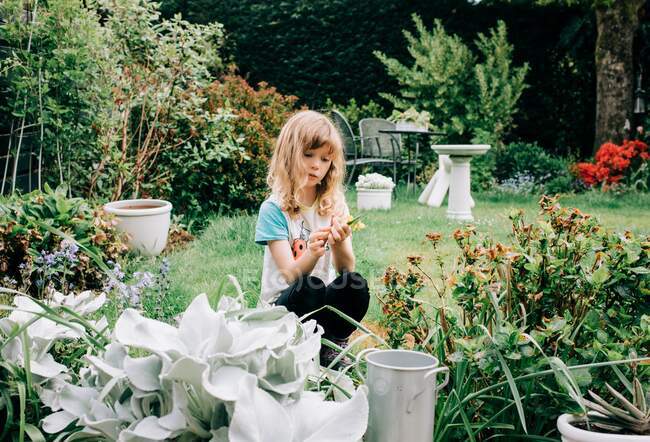 Chica sentada en un hermoso patio trasero recogiendo flores buscando reflexivo - foto de stock