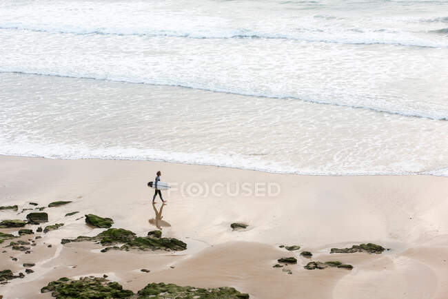Um homem caminhando pela areia na praia com sua prancha de surf — Fotografia de Stock
