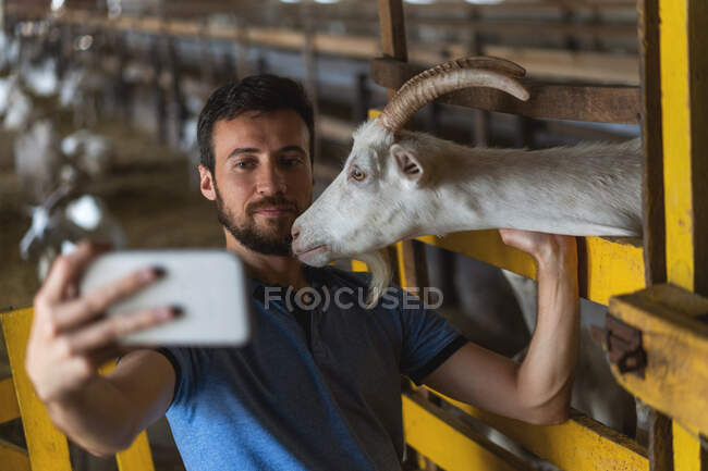 Tipo tira uma selfie ao telefone com uma cabra — Fotografia de Stock