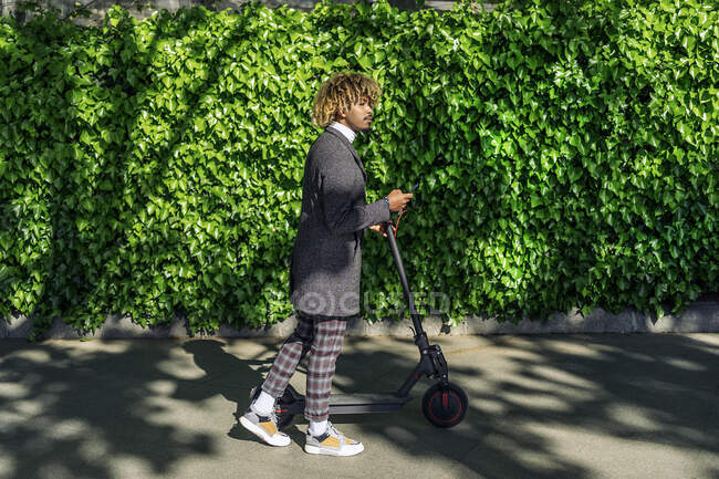 Африканский человек ходить с помощью мобильного телефона и электрического скутера на улице в зеленом фоне — стоковое фото