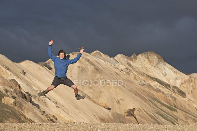 Adolescente saltando frente a las montañas de Landmannalaugar / Islandia - foto de stock