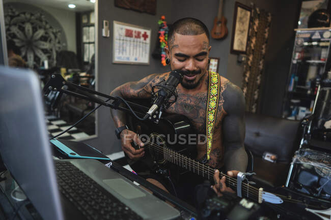 Татуировщик все в татуировках играет на гитаре и поет в тату — стоковое фото