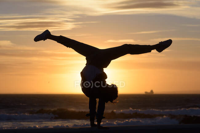 Una chica haciendo acrobacias con el sol en el fondo - foto de stock