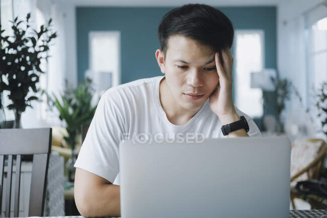 Thoughtful serious young man solving online problem doing resear — Stock Photo