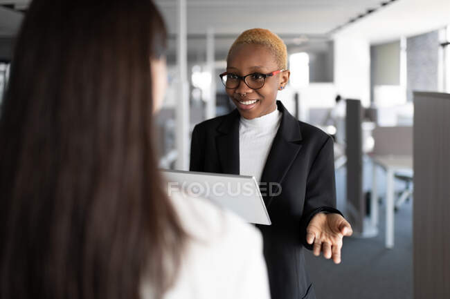Glücklicher schwarzer Mitarbeiter lächelt und diskutiert mit Kollegen im Büro über Daten auf dem Tablet — Stockfoto