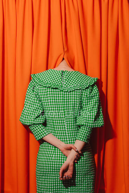 Chica en un vestido verde escondiendo su cabeza en cortinas naranjas - foto de stock