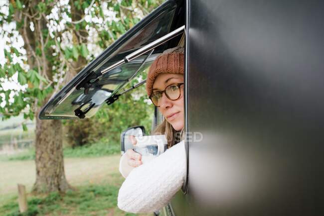 Woman looking out the window of her camper enjoying a cup of coffee — Stock Photo