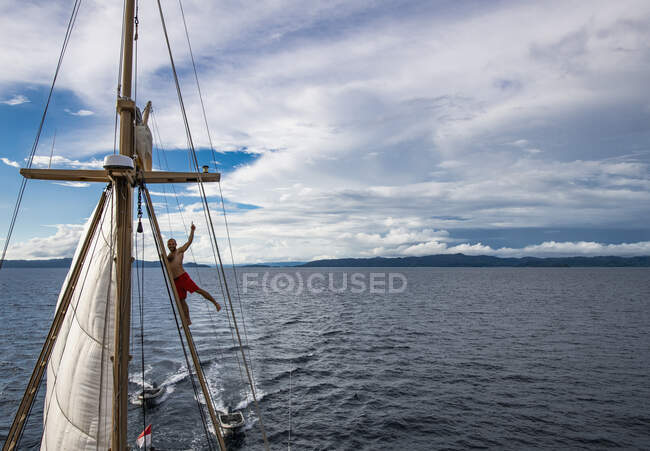 Man in board shorts climbing up rigging of sail boat in Raja Ampat — Stock Photo