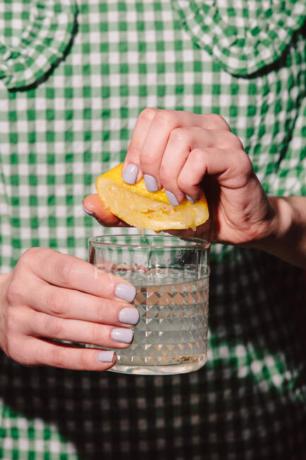 As mãos de mulher que apertam um limão em um copo — Fotografia de Stock