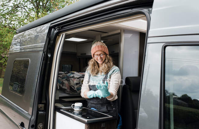 Woman putting rubber gloves on in her camper van washing up happily — Stock Photo