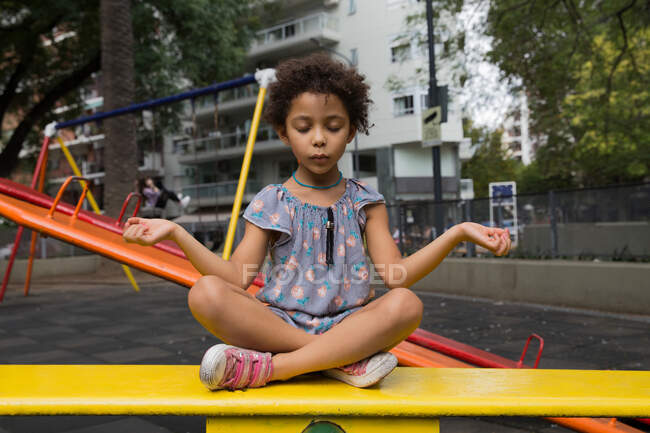 Liebenswertes Mädchen mit gemischter Rasse übt Meditation auf einem Spielplatz im Freien — Stockfoto