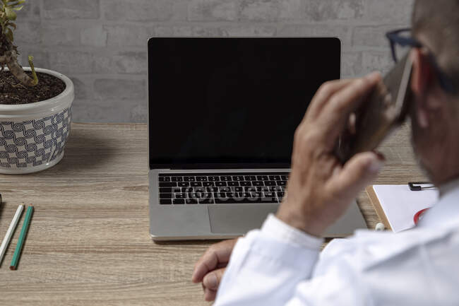 Médico trabalhando com laptop enquanto fala no telefone — Fotografia de Stock