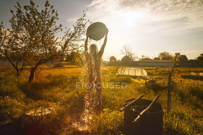 A man pouring ice water from a bowl at dawn in a field. — Stock Photo