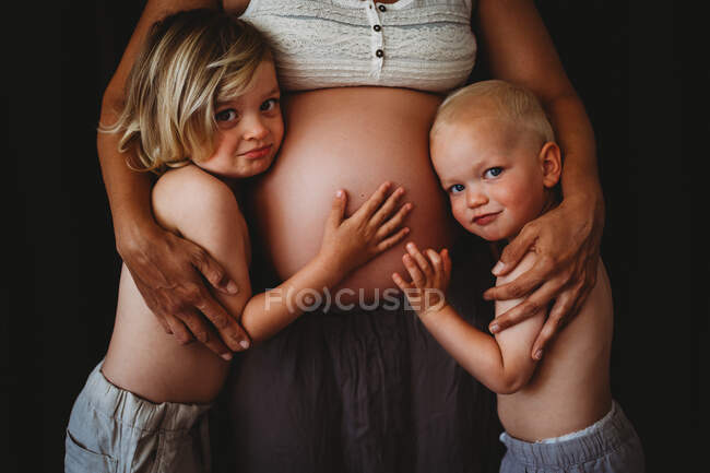 Jovens meninos tocando a barriga grande grávida da mãe olhando para a câmera — Fotografia de Stock