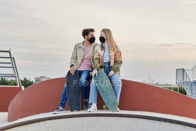 Casal jovem em máscaras olhando um para o outro em um parque de skate — Fotografia de Stock