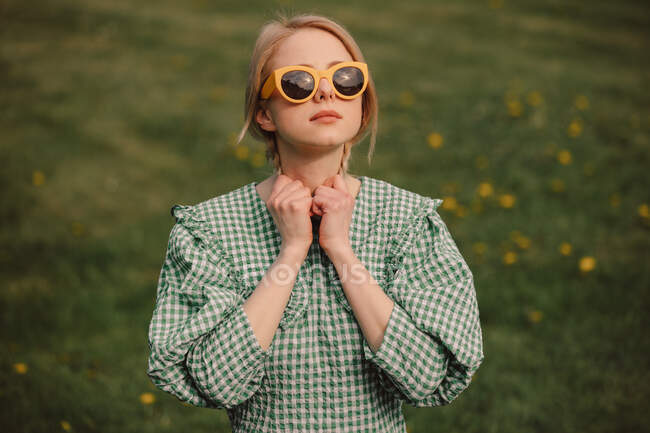 Style blonde en lunettes de soleil jaunes et robe verte sur une prairie — Photo de stock