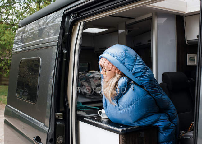 Woman sat enjoying a cup of coffee in her sleeping bag in her camper — Stock Photo