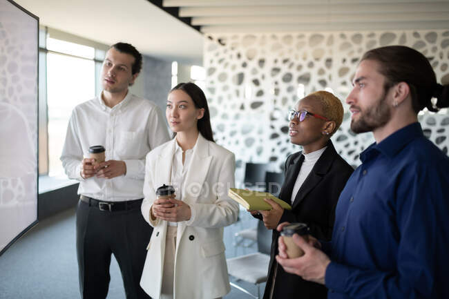 Diversos homens e mulheres com bebidas para ir e planejador fazendo videochamada no escritório — Fotografia de Stock