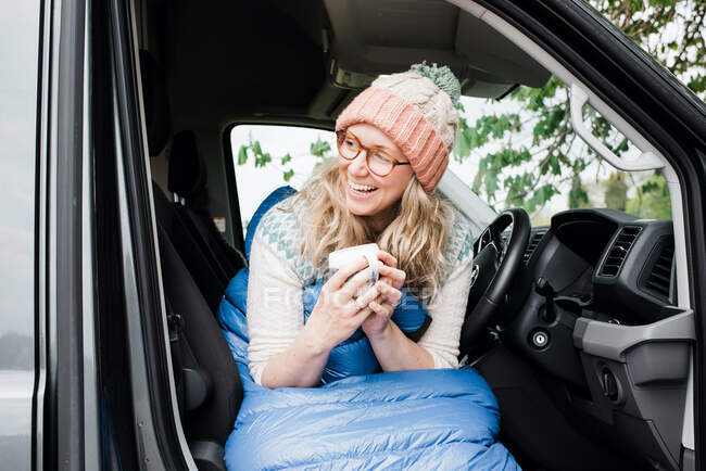 Femme assise dans son van riant le matin avec une tasse de café — Photo de stock