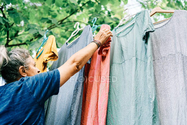 Mujer cuelga coloridos vestidos en perchas en tendedero en el jardín casero - foto de stock