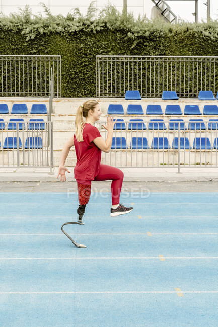 Sportive à corps complet avec jambe prothétique en course sur piste près de l'hippodrome pendant l'entraînement de remise en forme sur le stade — Photo de stock