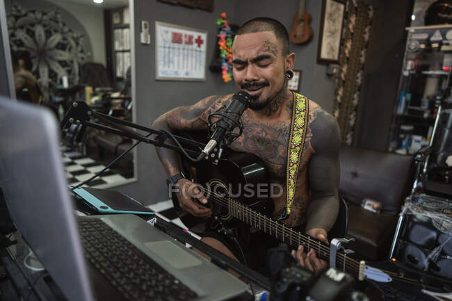 Tatoueur gars tous dans tatouages joue de la guitare et chante dans le tatouage — Photo de stock