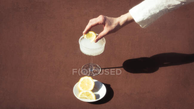 Weibliche Hand presst eine Zitrone in einen alkoholischen Cocktail — Stockfoto