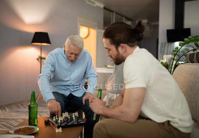Uomo anziano che gioca a scacchi con giovane ragazzo mentre cerca di combattere la demenza a casa — Foto stock