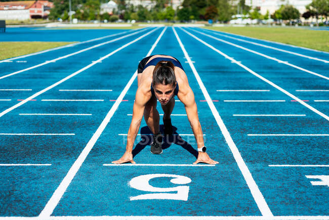 Mulher atleta em campo de corrida na posição inicial — Fotografia de Stock