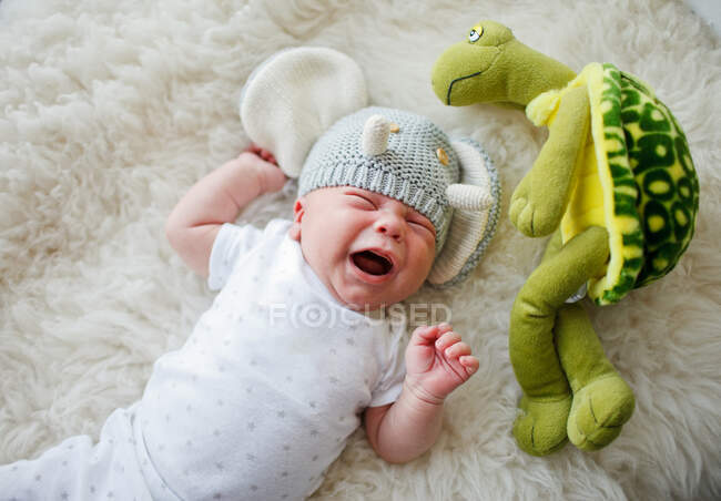 Un recién nacido en un sombrero divertido se acuesta y llora - foto de stock