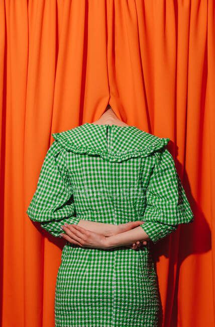 Menina em um vestido verde escondendo a cabeça em cortinas laranja — Fotografia de Stock