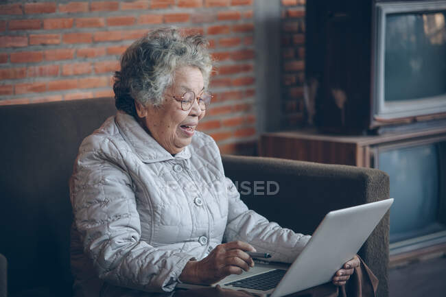 Sorridente donna anziana onda alla fotocamera avendo videochiamata sul computer portatile, — Foto stock