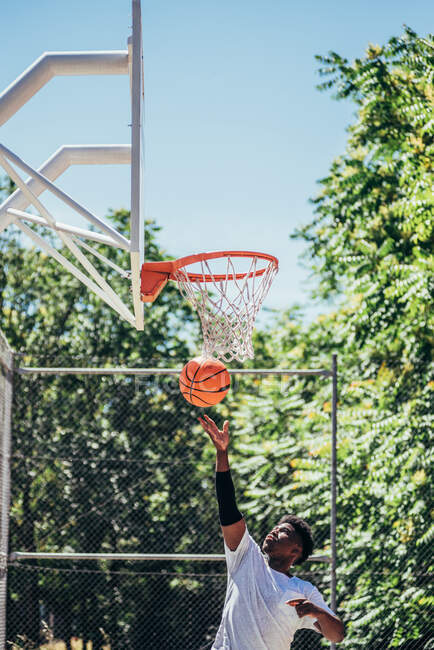Retrato de un afro negro saltando a la canasta para disparar la pelota. Jugar baloncesto en una cancha urbana. - foto de stock