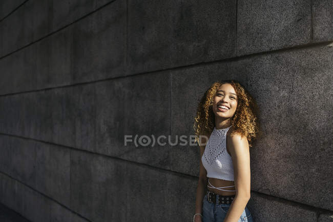 Stock photo of portrait of young blonde curly girl against the wall. She has confident attitude and looking at camera. She is wearing casual clothes — Stock Photo