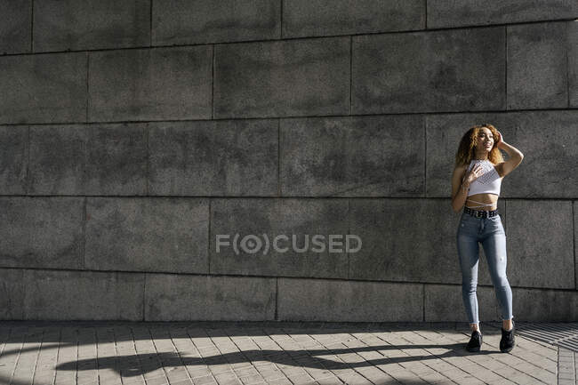 Stock photo of portrait of young blonde curly girl against the wall. She has confident attitude. She is wearing casual clothes - foto de stock