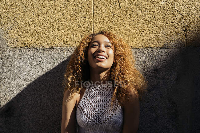 Foto stock de retrato de menina encaracolada loira jovem contra a parede. Ela tem atitude confiante e olhando para a câmera. Ela está vestindo roupas casuais — Fotografia de Stock