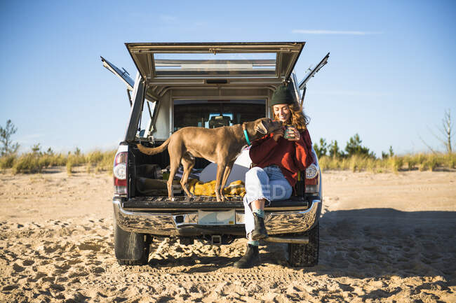 Jovem mulher com seu cão bebendo café na praia — Fotografia de Stock