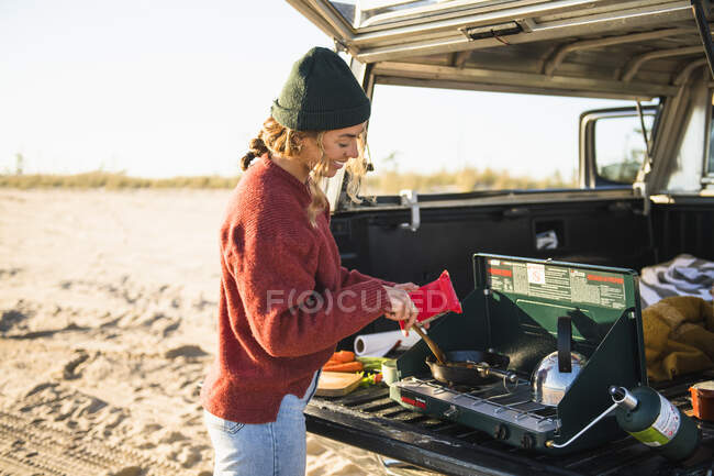 Молодая женщина задней кулинарии в то время как пляжный автомобиль кемпинг в одиночку — стоковое фото
