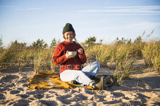 Mujer joven disfrutando de la sopa mientras coche de playa camping solo - foto de stock