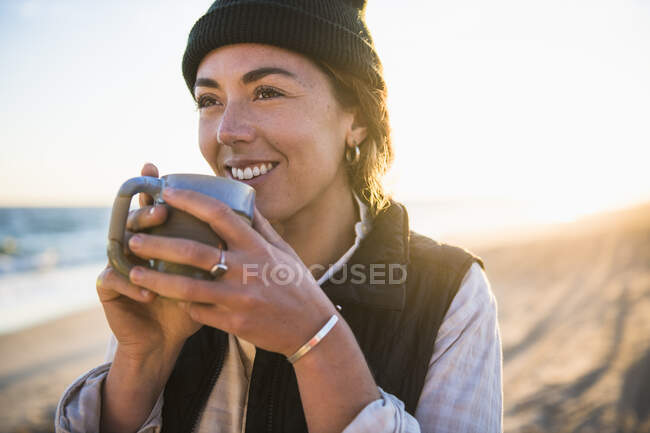 Молода жінка з чашкою п'є каву на пляжі — стокове фото