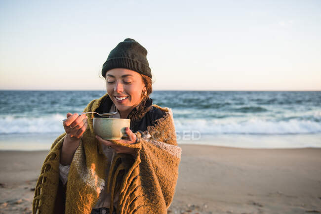 Молодая женщина наслаждается миской супа, в то время как пляж автомобиль кемпинг осенью — стоковое фото