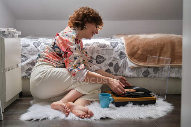 Молодая женщина ставит виниловую пластинку на проигрыватель в своей спальне — стоковое фото