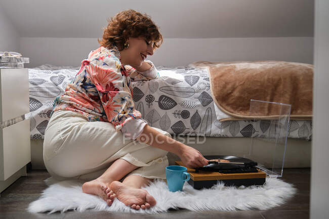 Joven mujer audiófila tocando música en un tocadiscos en su dormitorio - foto de stock