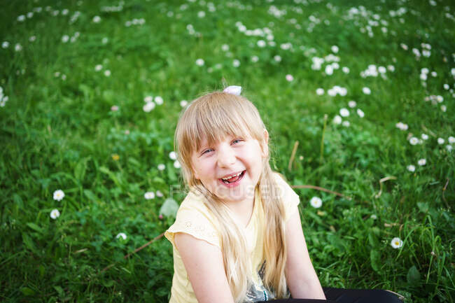 Menina loira ri no campo com margaridas — Fotografia de Stock