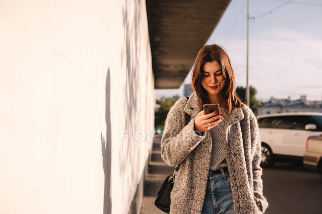 Mulher feliz usando telefone inteligente andando na rua na cidade — Fotografia de Stock