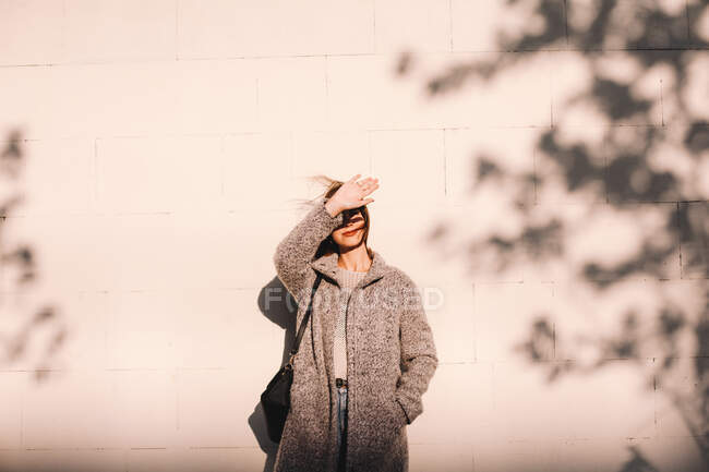 Young woman shielding eyes standing against wall in city — Stock Photo
